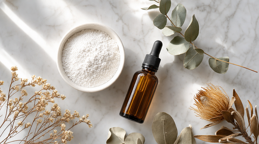 Natural mineral skincare ingredients flat lay — zinc oxide powder in ceramic bowl with botanical oil and native wildflowers on white marble