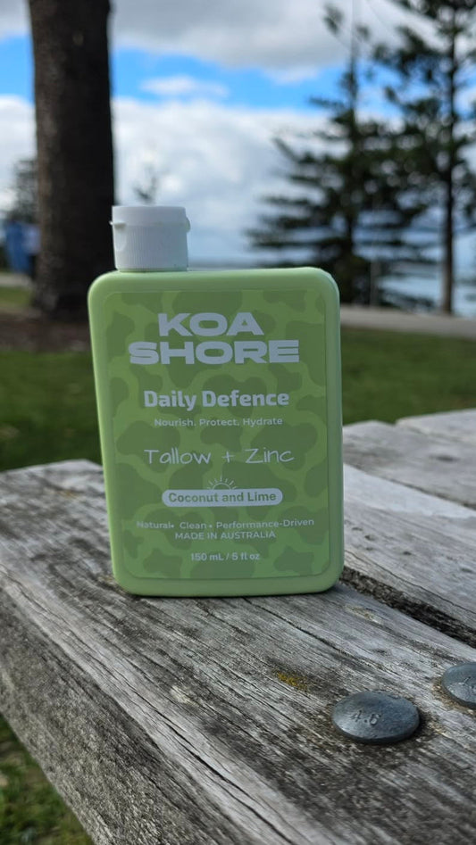 Koa Shore Daily Defence bottle on a timber bench by the coast