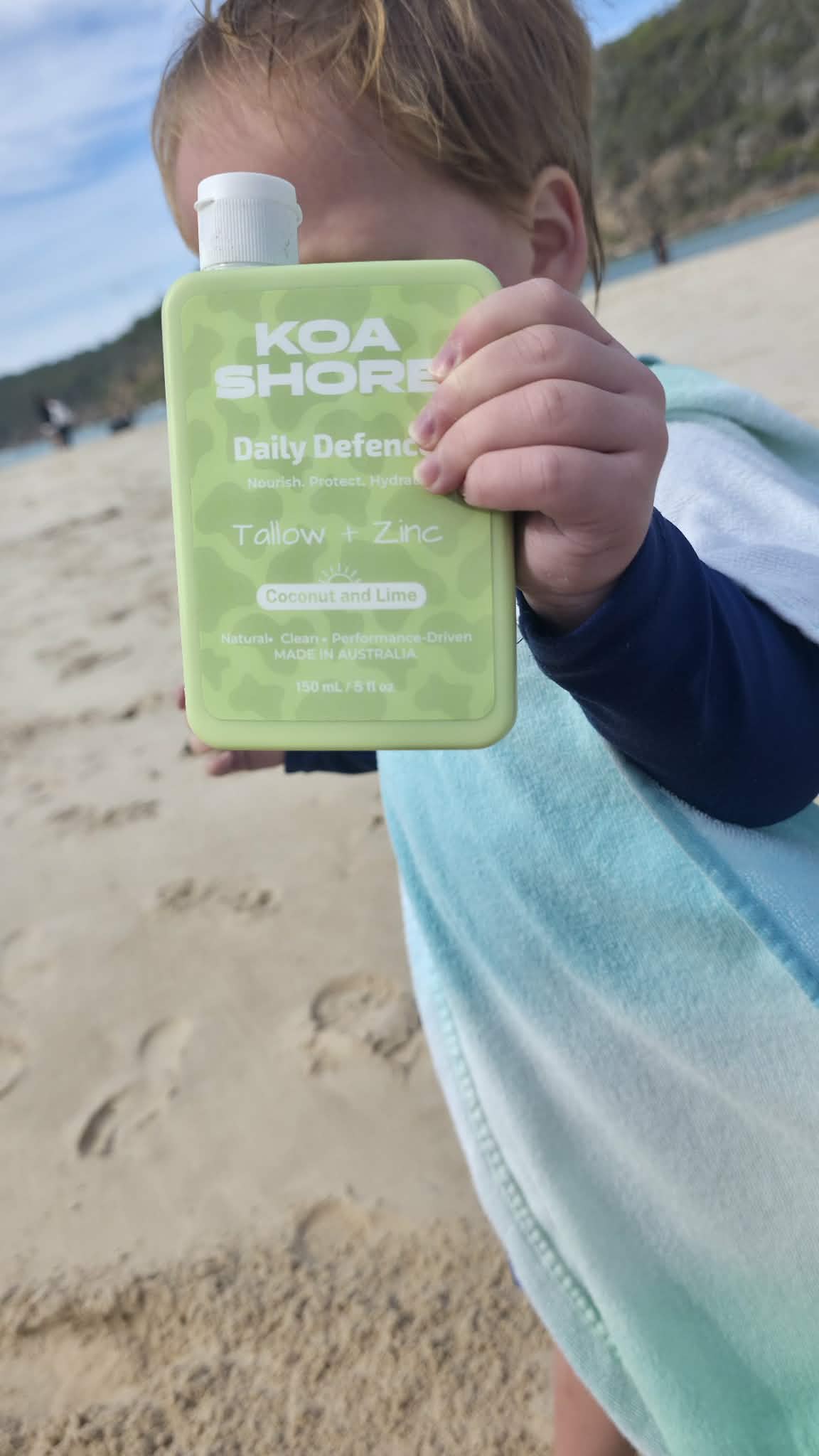 Koa Shore Daily Defence Coconut Lime bottle held at the beach