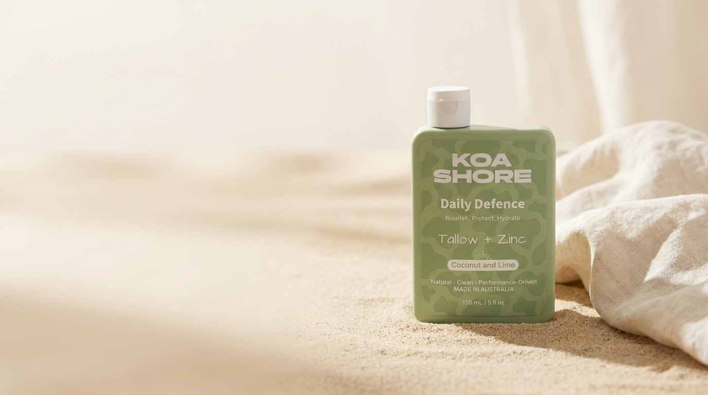 Koa Shore Daily Defence Coconut and Lime bottle on warm sand beside a linen towel, soft coastal light